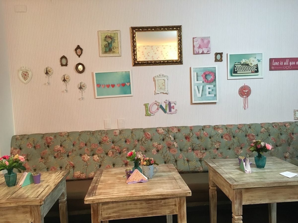 Salão da confeitaria com sofá florido, mesinhas de madeira e quadros na parede